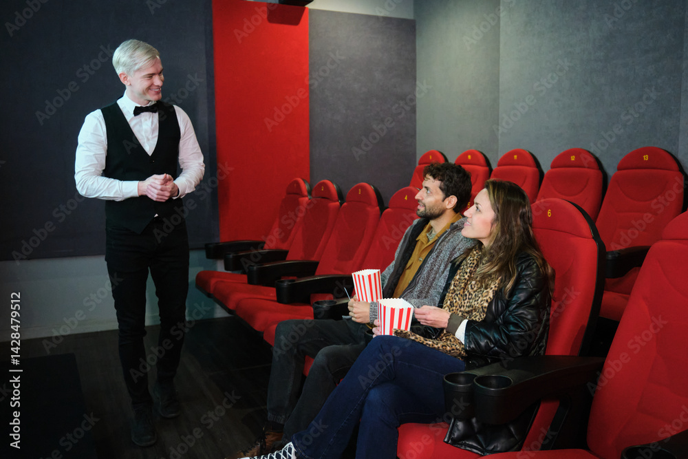 Couple sitting in movie theater enjoying popcorn while usher welcomes them