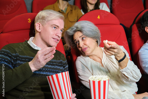 Man and woman sharing their impressions while watching film in movie theater