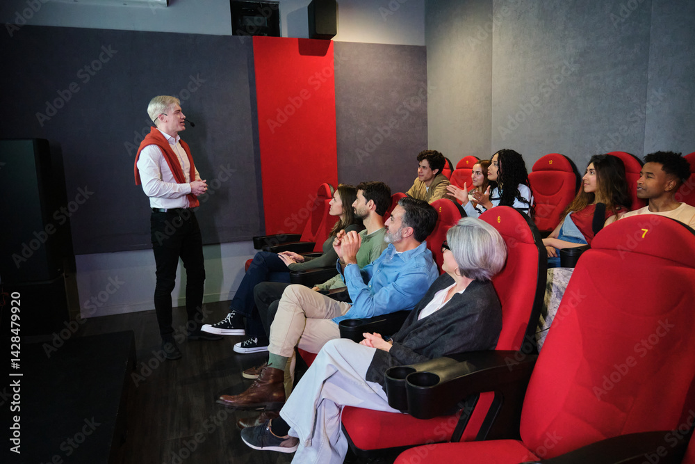 Speaker giving presentation to audience sitting on red chairs in conference room