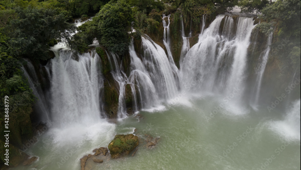 Fototapeta premium Multiple Waterfalls Cascading into a Pool Surrounded by Lush Greenery