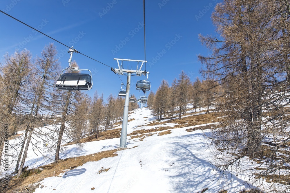 Obraz premium Ski lift on snowy mountain with blue sky and pine trees in winter landscape