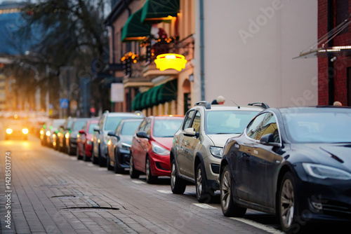 Obraz na płótnie Cars parked in row. Vehicles tightly parked along a narrow city street at dusk, illustrating the everyday struggle of finding free parking space in crowded urban neighborhoods and downtown areas. w salonie