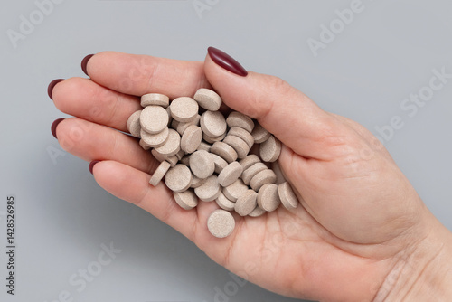 Cupped womans hand with a pile of beige medical pills top view over grey