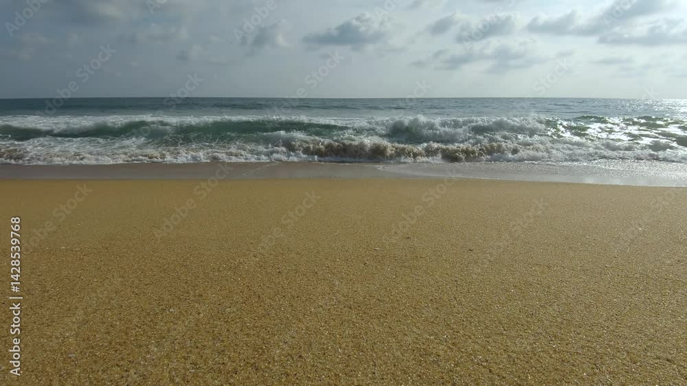 Ocean waves crashing on a sandy beach under a cloudy sky on a sunny summer day Ocean waves crashing on a sandy beach under a cloudy sky on a sunny summer day