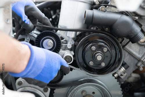 Mechanic Working on Car Timing Belt Replacement Under the Hood in Automotive Workshop