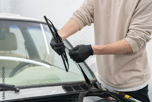 A person is changing car wiper blades while wearing gloves to ensure cleanliness and safety in a garage workspace.