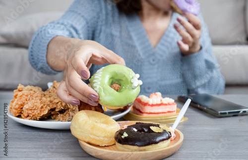 woman’s hand reaches for a donut on table that full of junk food like fried chicken, cake, sweet drinks, and desserts, showing signs of sugar addiction, eating too much, and eating unhealthy food  photo