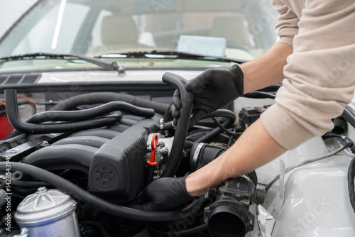 Mechanic works on installing air hose inside the engine compartment of a vehicle, ensuring proper function at an auto repair shop.