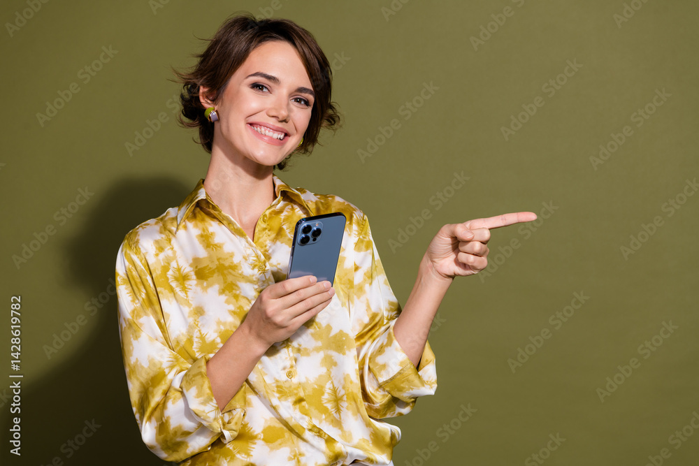 Confident young businesswoman with smartphone pointing right, against khaki backdrop, conveying modern communication and professionalism