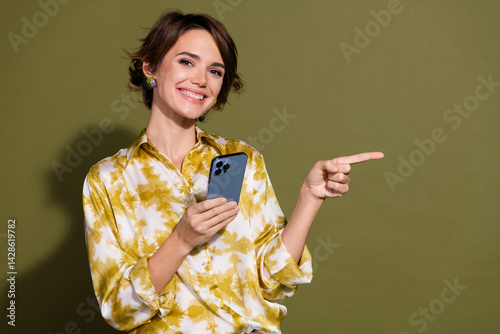 Obraz na płótnie Confident young businesswoman with smartphone pointing right, against khaki backdrop, conveying modern communication and professionalism w salonie