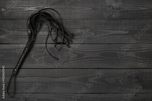 Black whip on wooden background, top view. BDSM concept