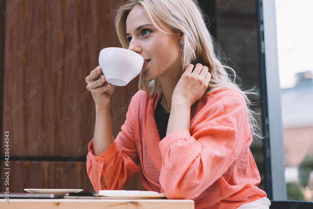 Young smiling businesswoman drinking coffee in cafe during remote work