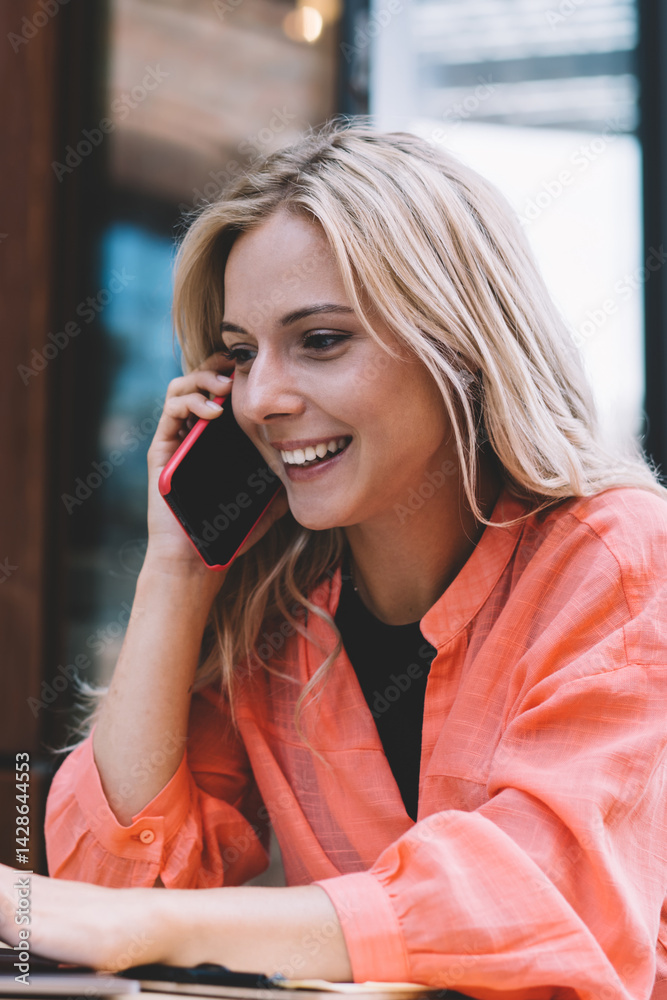 Positive young businesswoman speaking on smartphone during remote work in cafe