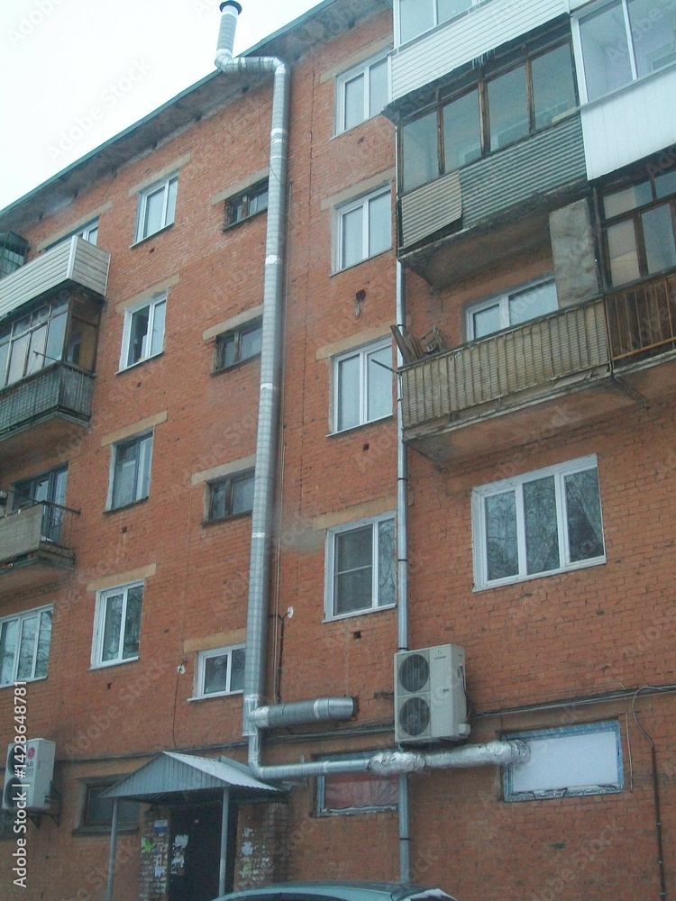 Fototapeta premium Unusual industrial pipe installation on a residential building in a snowy urban environment