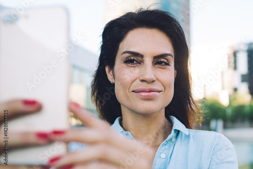 Obraz na płótnie Beautiful brunette woman 30s using mobile phone for making selfie on modern architecture urban setting background,charming female blogger taking photo on smartphone camera using app and 4G connection w salonie