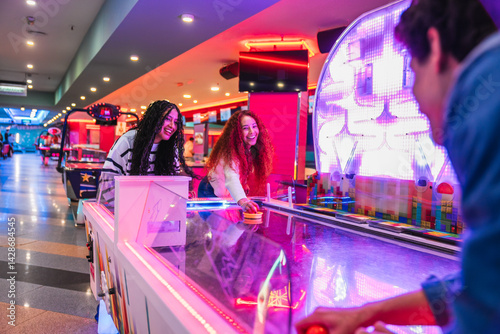 Cheerful young friends enjoying a competitive game of air hockey in a vibrant entertainment center, showcasing the excitement and fun of arcade gaming