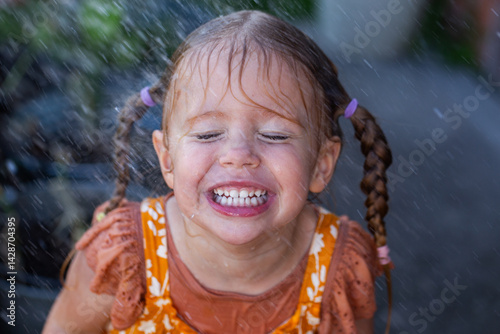 Happy little girl outside with droplets of water raining down on face