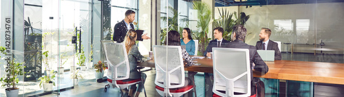 Office business team talking at big meeting table in modern conference room, brainstorming in coworking space with large glass wall, window, leader talking to colleagues, group planning new project 