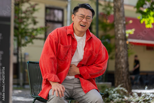 Foto Asian middle-aged man feeling sudden strong abdominal stomach ache, gastritis problem outdoors