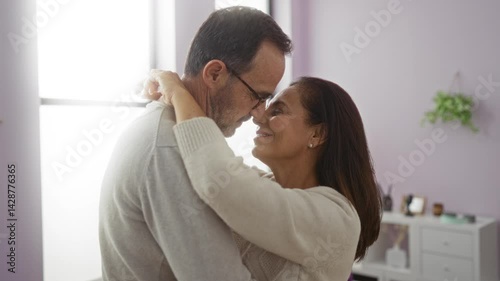 Middle-aged hispanic couple embracing lovingly in a bright living room suggests warmth and affection.