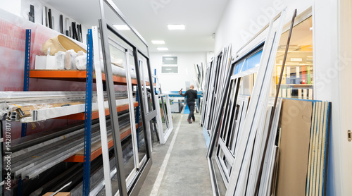 Carpenter walking in workshop with aluminum window frames and shelving