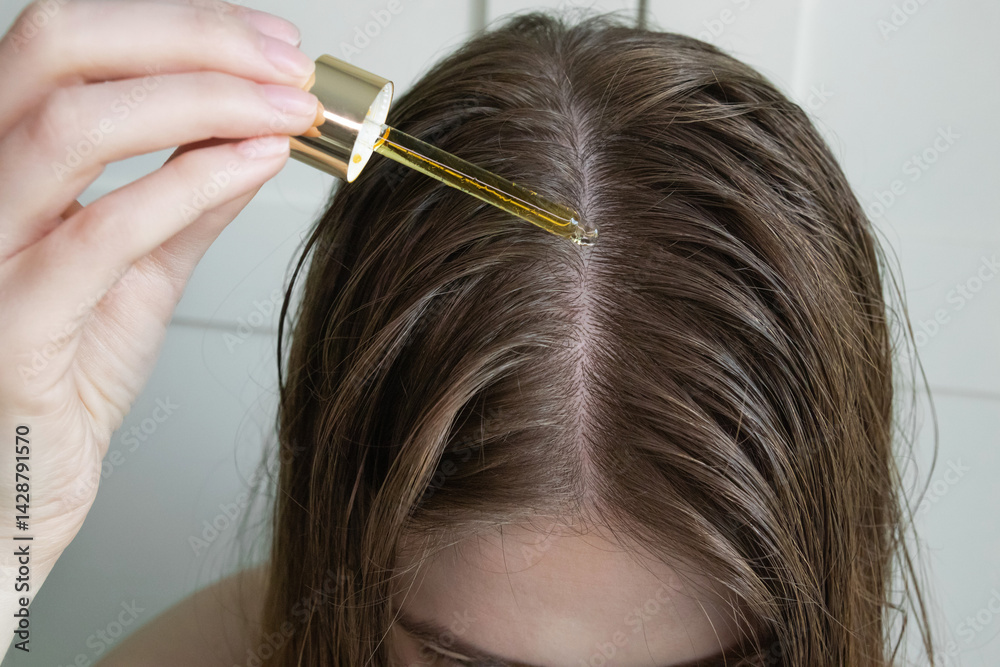 Fototapeta premium Close up of young woman applying hair growth oil to scalp with dropper after washing hair. Treatment for hair loss prevention, scalp care, and hair regrowth.