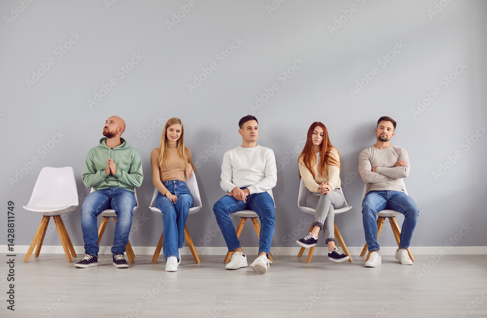 Naklejka premium Young people men and women in casual clothes sitting on chairs in row waiting for interview invitation turn in office. Job candidates seekers sitting on gray wall background. Recruitment concept.