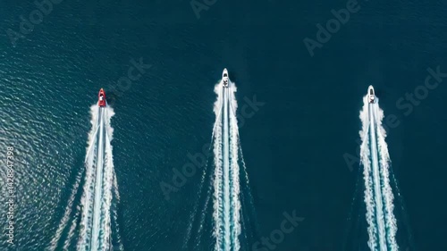 Aerial view of three boats racing on the water leaving white wakes