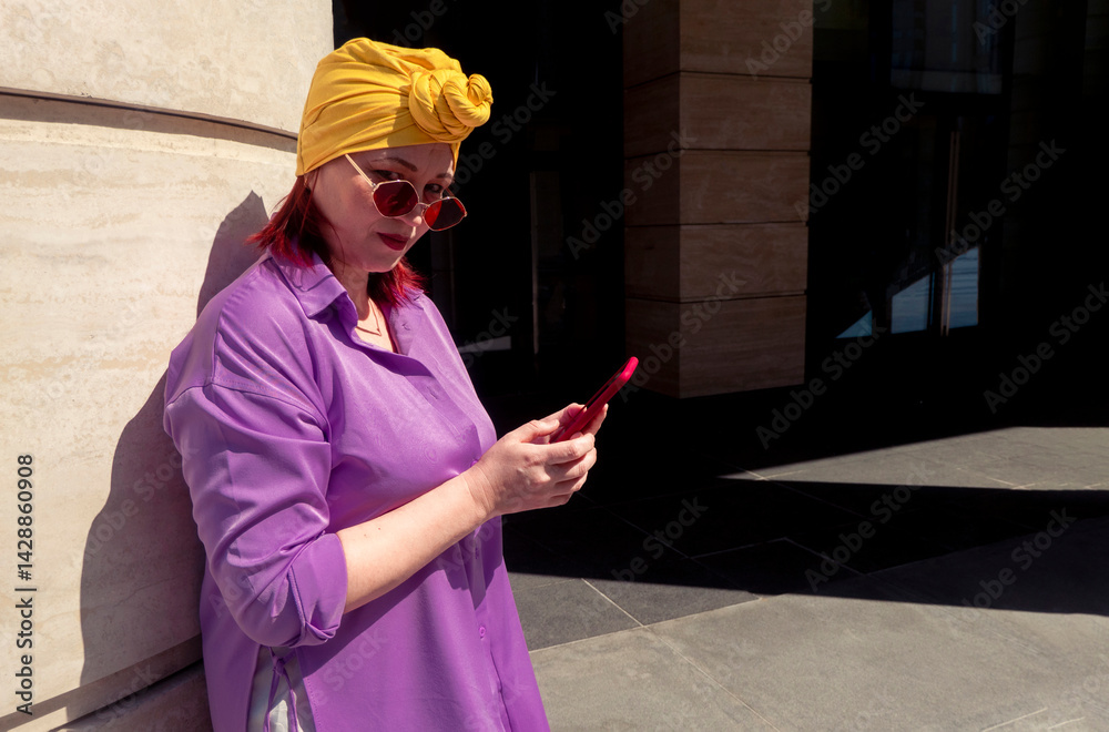 Happy and funny cool lady with fashionable clothes on dark background look to the phone seriously and thoughtfully - adult asian with extravagant style, concepts about lifestyle, fasion and elderly