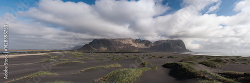 Obraz na płótnie Wide-angle shot of Vestrahorn mountains emerging from mist with soft light illuminating black sand dunes and sparse vegetation on the Icelandic coast. w salonie