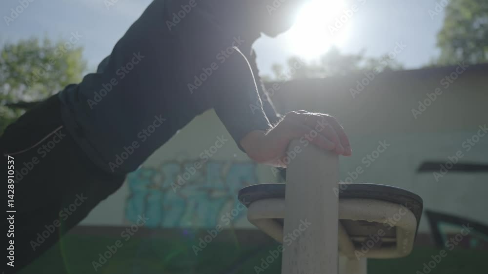 Man doing push ups on street fitness equipment with sunlight in background. Outdoor workout session. Active lifestyle, sport and fitness concept