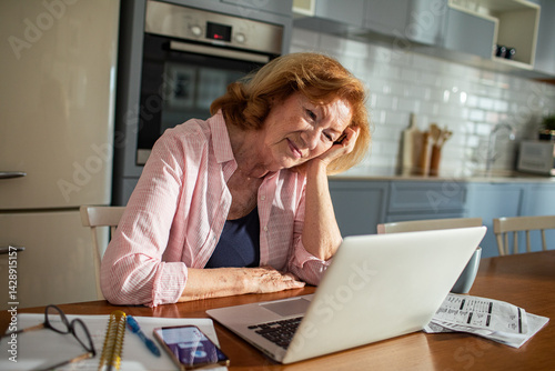 Senior woman managing bills at home with laptop