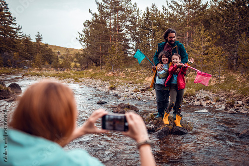 Family taking photo by mountain stream with kids holding nets on nature adventure photo