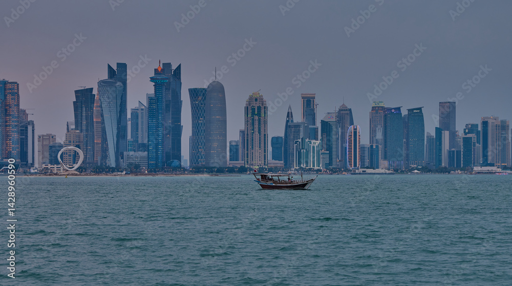 Fototapeta premium Doha Qatar skyline from corniche promenade sunset shot showing dhows in Arabic gulf with Qatar flag