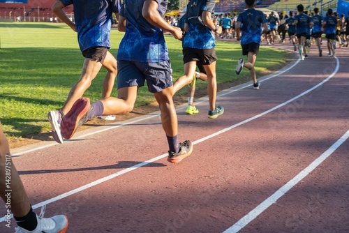 Group of athletes running on a track field in the morning, focus on legs and shoes, outdoor sports training, active and healthy lifestyle.