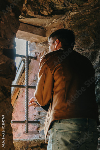 A young man looks at the landscape through an ancient window in a castle.
