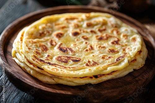Close-up of a freshly cooked roti with a golden-brown, crispy texture, placed on a wooden plate with a side of curry