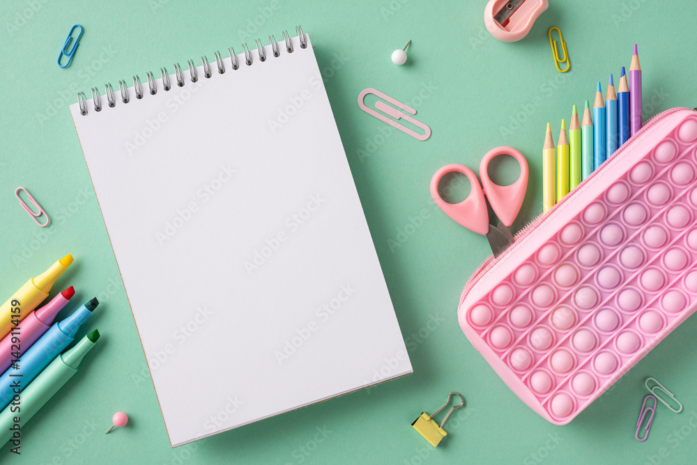 Colorful notepad, pens, pencils, and stationery neatly arranged on a green surface Colorful notepad, pens, pencils, and stationery neatly arranged on a green surface