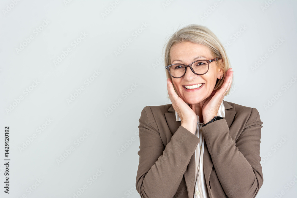 Happy mature businesswoman smiling while standing against a light grey wall, looking confident and relaxed. Professional, successful, and positive attitude concept. Happy mature businesswoman smiling while standing against a light grey wall, looking confident and relaxed. Professional, successful, and positive attitude concept.