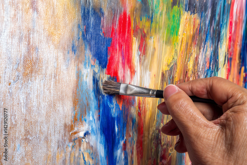 The image shows a close-up of a hand holding a paintbrush, applying strokes to a colorful, abstract painting on a canvas