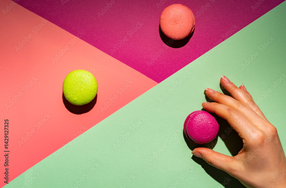 Cookie macaron or macaroon with womans hand on colorful bright background from above. Multicolored almond cookies with bright shadows, top view
