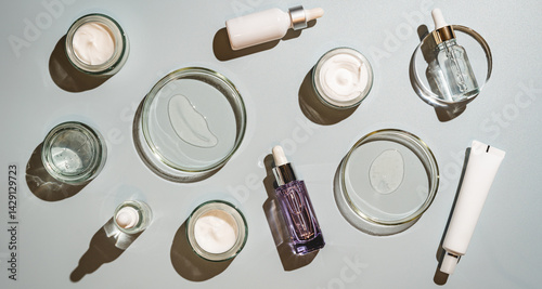 Different glass bottles with serum or oil and cosmetic skin care cream on gray background. Trending shadow. Cosmetic mockup. Top view with copy space. Flat lay.