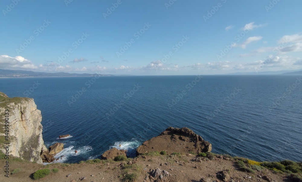 Beautiful blue ocean with a rocky cliff in the background. The water is calm and the sky is clear