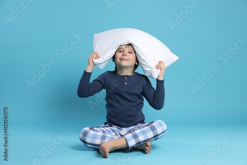 Cute boy with pillow on light blue background