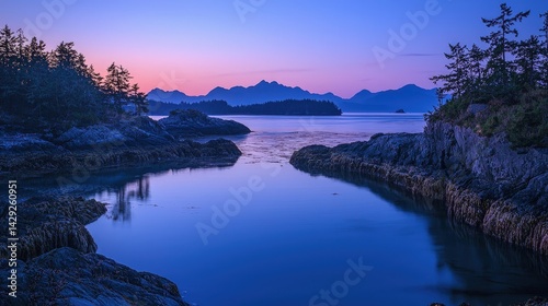 Serene inlet with reflective blue water, silhouetted evergreen trees, rocky shores, and mountain landscape at dusk