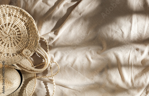 Summer essentials on linen tablecloth background. Flat lay of straw hat and bag in gentle sunlight. Copy space for product. Boho summer vibes. 