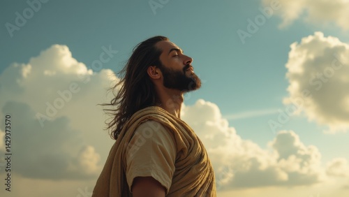 Obraz na płótnie Man with a beard and long hair is standing in the sun, looking up at the sky. He is wearing a robe and he is in a contemplative or meditative state w salonie