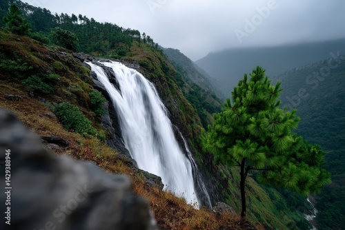 Majestic waterfall cascades through mountain terrain in misty weather