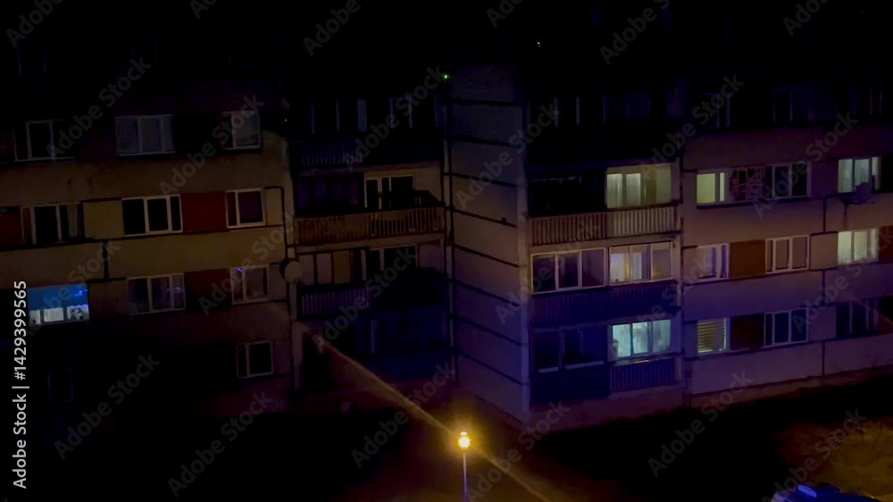 Soviet-era apartment block illuminated by blue and amber police vehicle lights at night