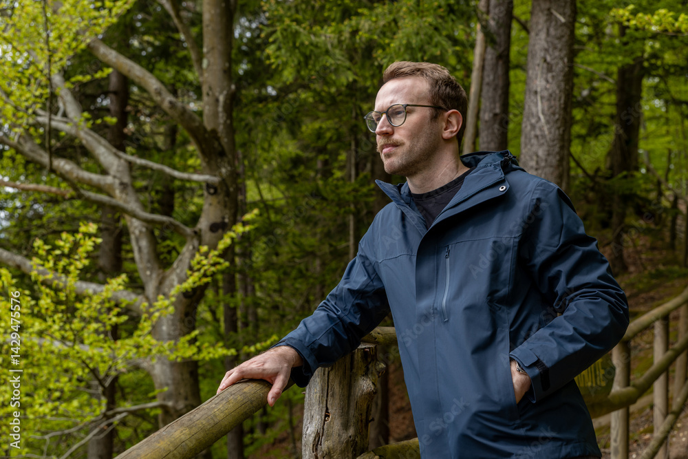 A young man in his thirties stands leaning on a wooden railing on a picturesque alpine path in spring in Austria A young man in his thirties stands leaning on a wooden railing on a picturesque alpine path in spring in Austria